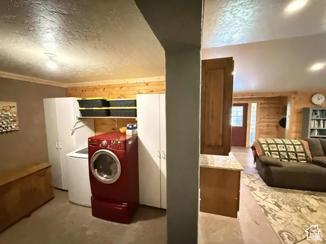 Laundry area with wood walls, a textured ceiling, washing machine and clothes dryer, and concrete flooring