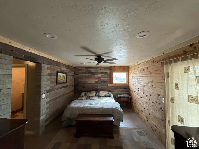Bedroom featuring a textured ceiling, wood walls, a ceiling fan, and tile patterned floors