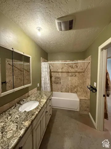 Bathroom featuring a textured ceiling, shower / bath combo, vanity, and concrete flooring