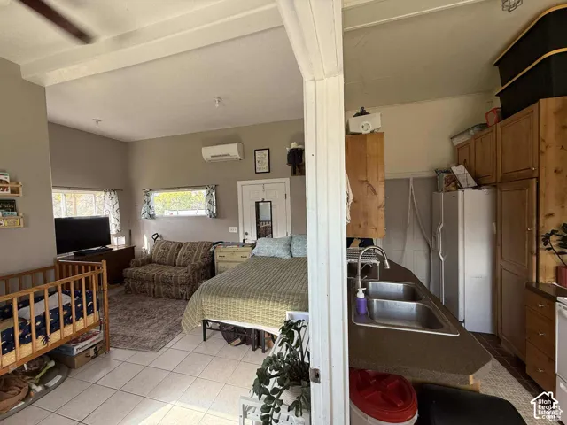 Bedroom with light tile patterned floors, white refrigerator with ice dispenser, and beamed ceiling