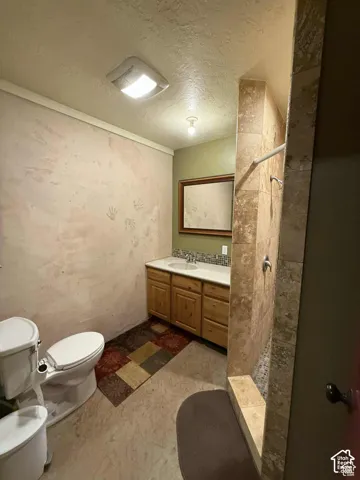 Bathroom with a tile shower, a textured ceiling, and vanity
