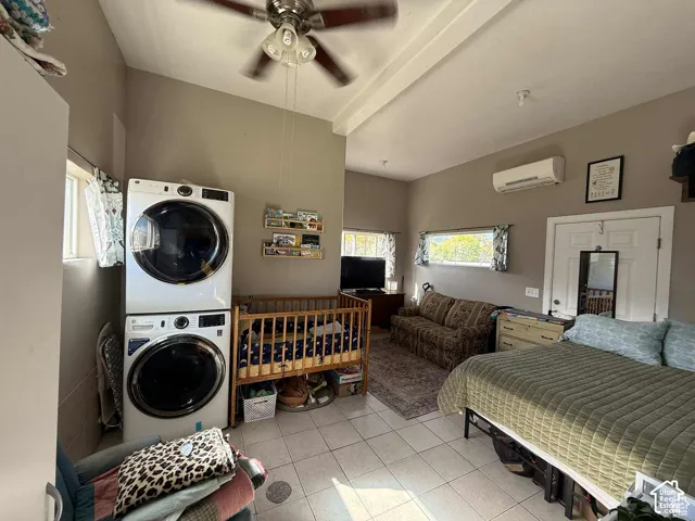 Laundry area featuring stacked washer and clothes dryer, light tile patterned floors, ceiling fan, and beam ceiling
