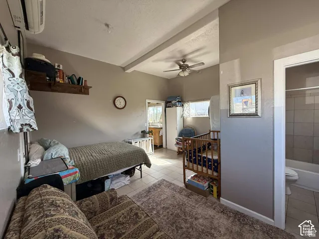 Bedroom featuring ensuite bath, light tile patterned floors, a textured ceiling, ceiling fan, and beamed ceiling