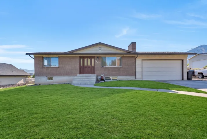 Ranch-style home with a front yard, a chimney, concrete driveway, a garage, and brick siding