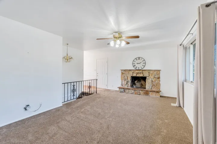 Unfurnished living room featuring ceiling fan, a fireplace, carpet floors, and a chandelier