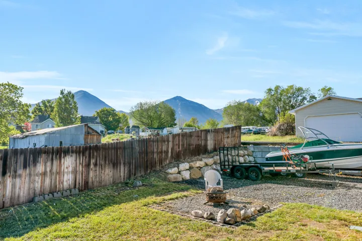 Fenced yard featuring a mountain view, a fire pit, a garage, and an outbuilding