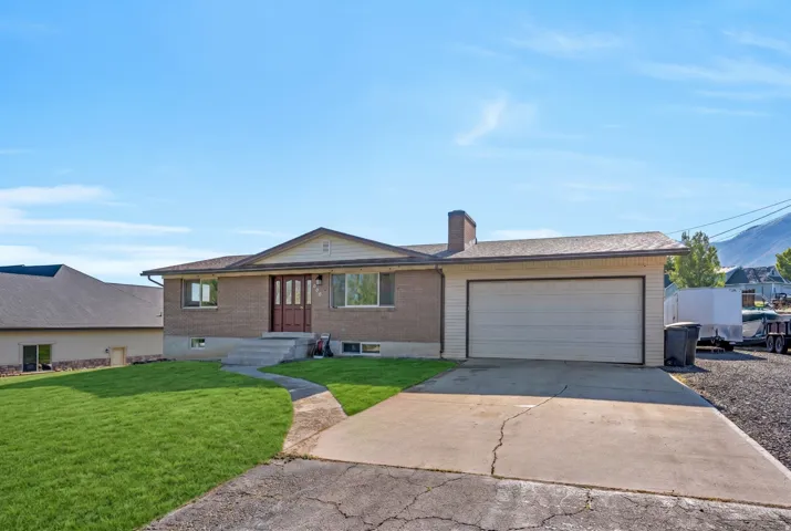 Ranch-style house featuring a front yard, brick siding, driveway, an attached garage, and a chimney
