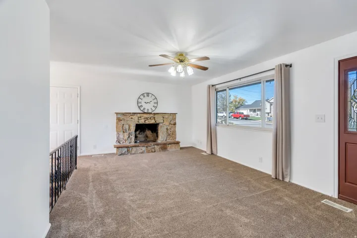 Unfurnished living room with a ceiling fan, carpet, and a stone fireplace