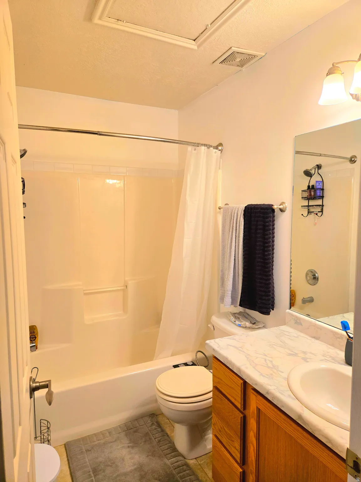 Full bath with vanity, shower / bath combo, a textured ceiling, and light tile patterned floors