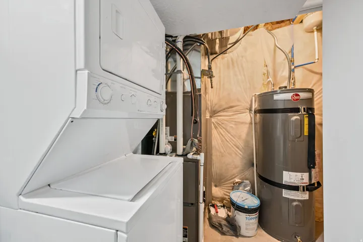 Laundry area featuring strapped water heater and stacked washer / drying machine