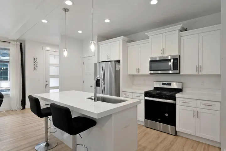 Kitchen featuring stainless steel appliances, white cabinetry, light wood finished floors, and a kitchen island with sink