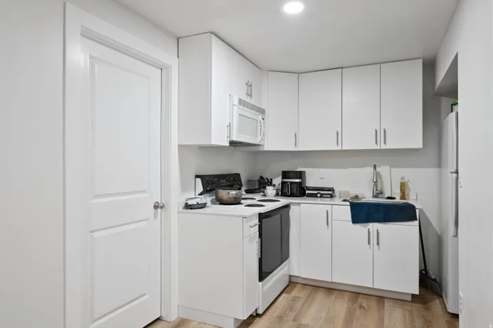 Kitchen featuring white appliances, light countertops, white cabinetry, light wood-style flooring, and recessed lighting