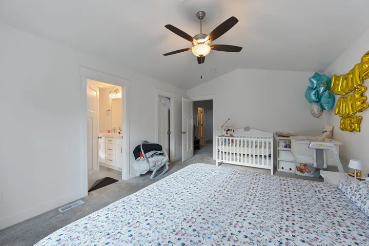 Bedroom with ceiling fan, lofted ceiling, light colored carpet, a crib, and ensuite bathroom