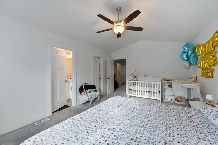 Bedroom featuring a ceiling fan, light colored carpet, vaulted ceiling, and a crib