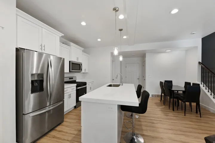 Kitchen featuring stainless steel appliances, an island with sink, white cabinets, and decorative light fixtures