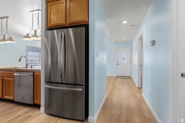 Kitchen with stainless steel appliances, wood finish cabinetry, light wood-type flooring, a textured ceiling, and recessed lighting