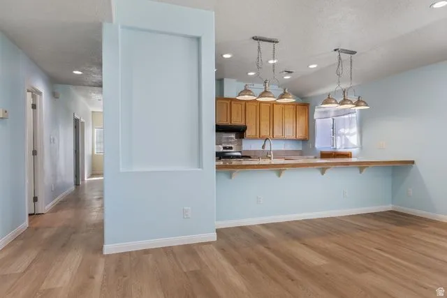 Kitchen featuring a kitchen bar, wood finish cabinetry, light wood finished floors, stainless steel range oven, and a peninsula