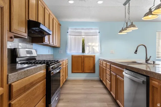 Kitchen with stainless steel appliances, pendant lighting, wood finish cabinets, light wood-style floors, and a textured ceiling