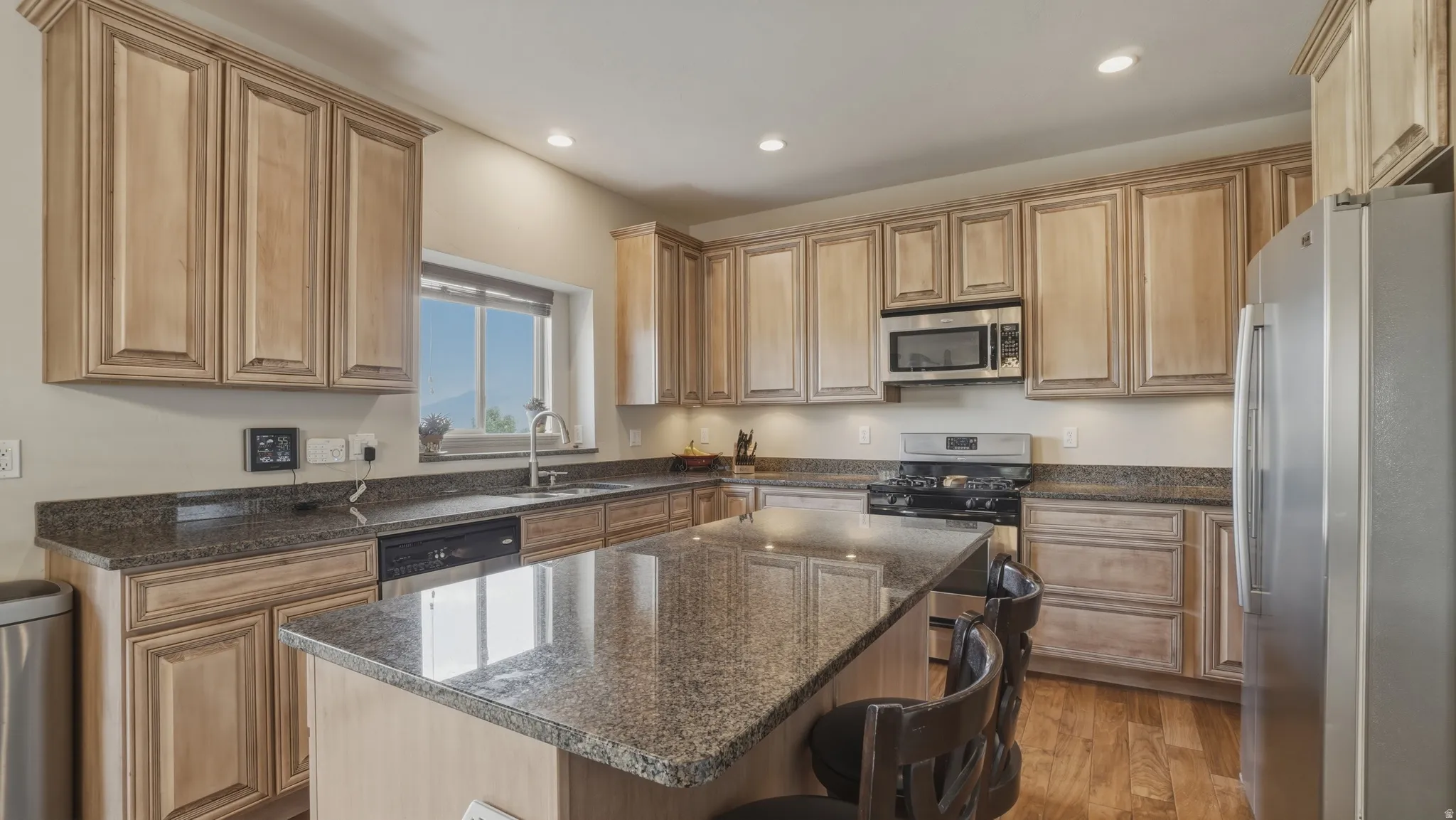 Kitchen with stainless steel appliances, dark stone countertops, a breakfast bar, dark wood-style floors, and recessed lighting