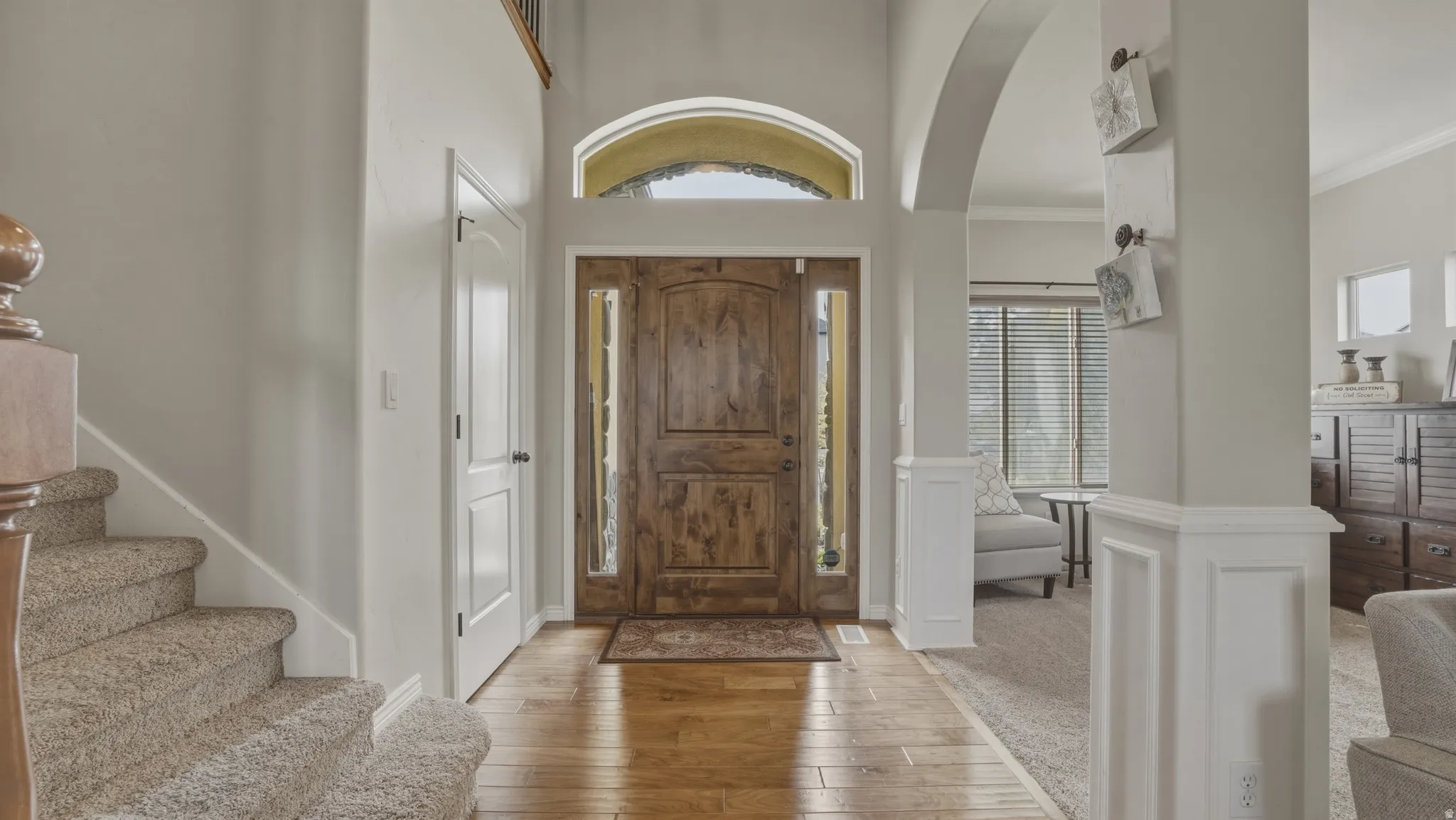 Foyer entrance featuring light wood-style flooring, arched walkways, ornamental molding, and a high ceiling