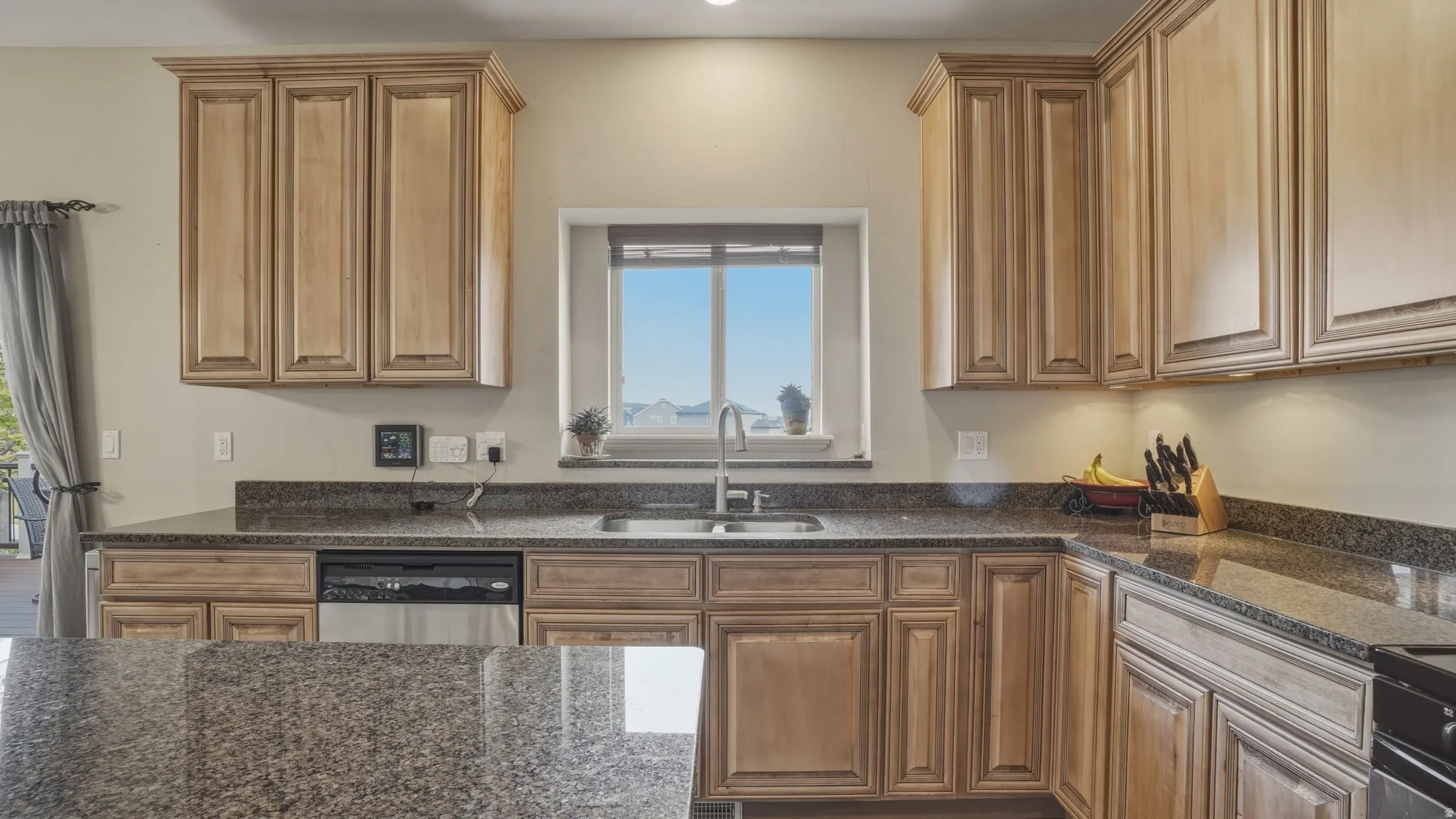 Kitchen featuring dark stone countertops, stainless steel dishwasher, and wood finish cabinetry