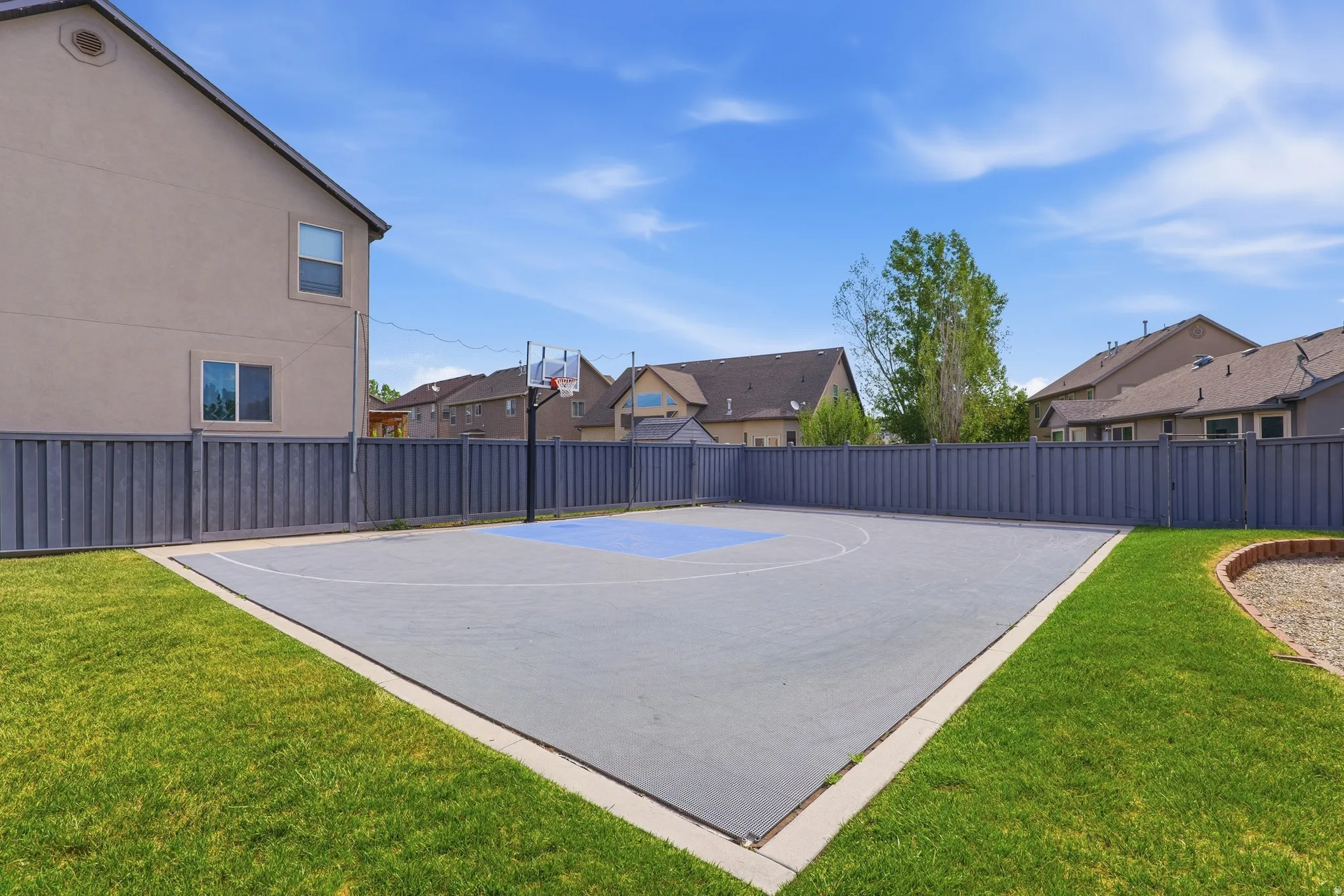 Expansive backyard featuring a concrete sport court with blue-painted markings and a basketball hoop
