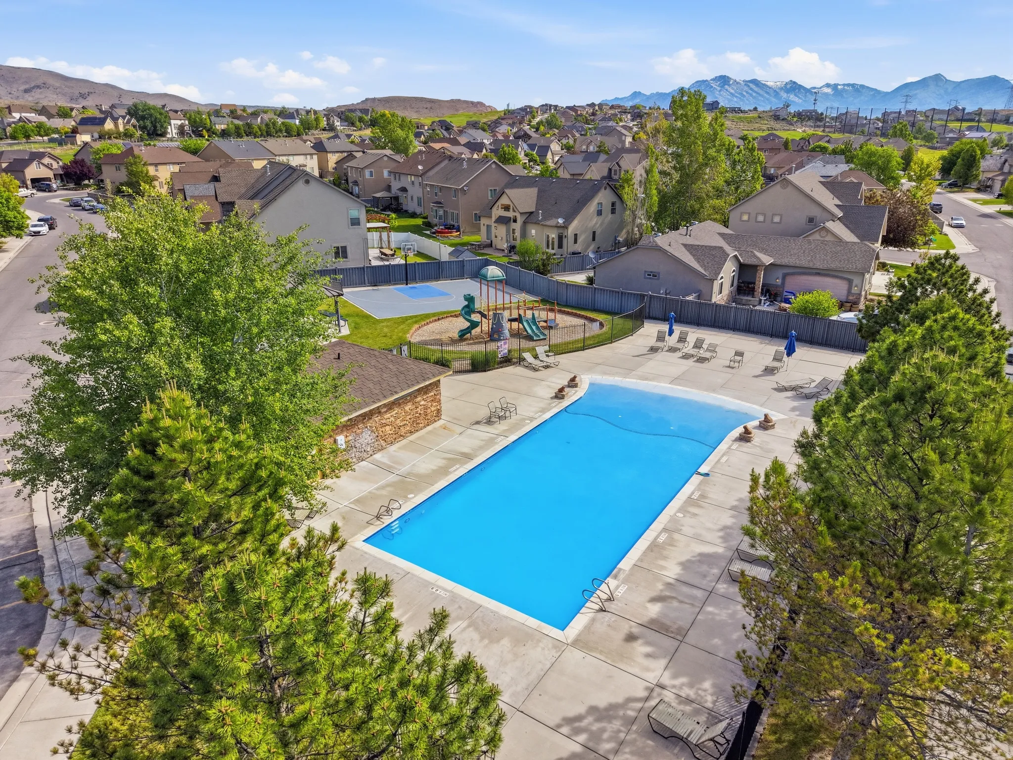 Community amenities featuring a rectangular swimming pool with surrounding concrete decking, a brick-clad amenity building, and a playground with a slide and climbing structure