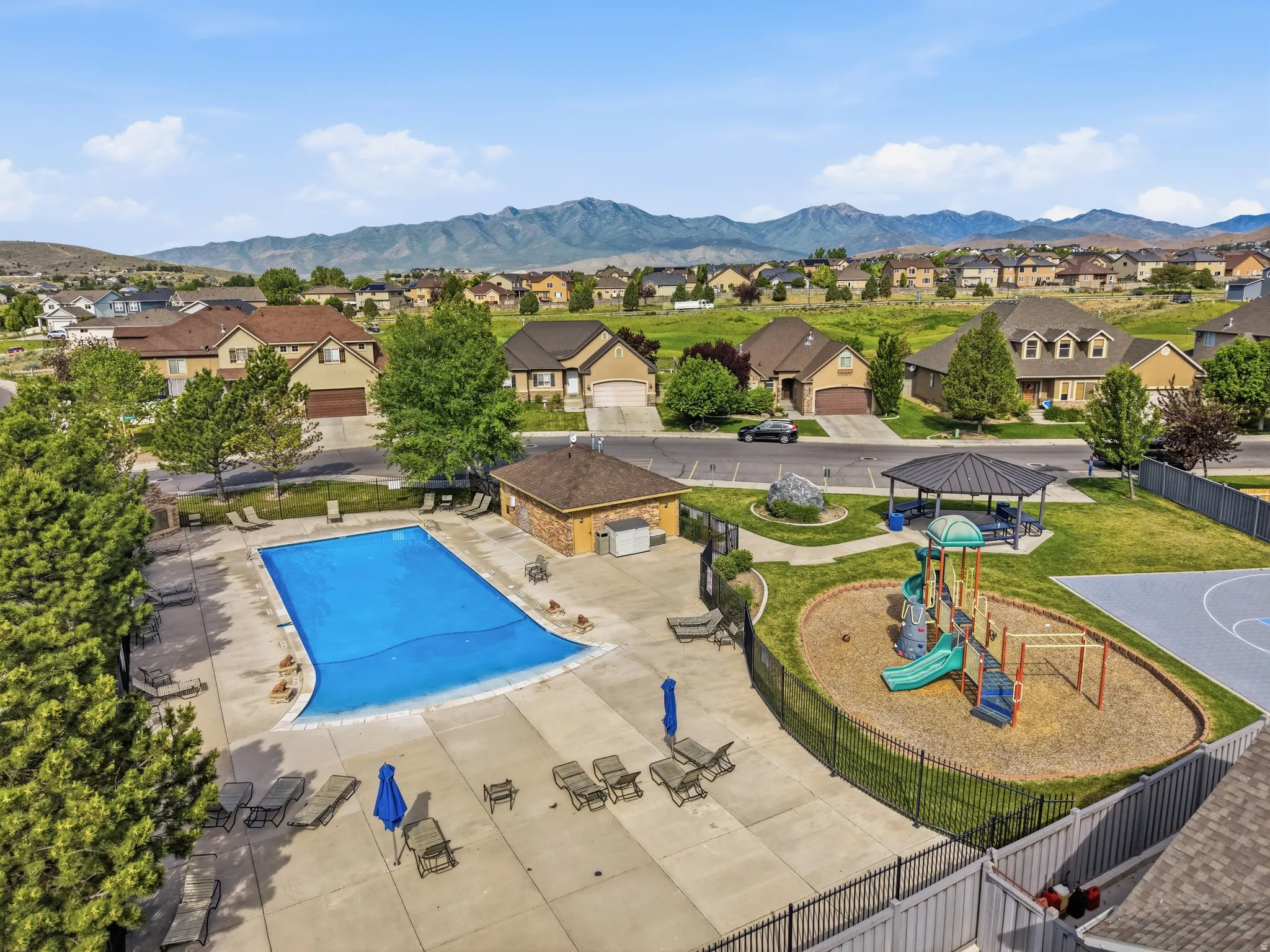Community amenities featuring a fenced swimming pool with surrounding concrete patio, adjacent playground with wood chip surfacing, covered picnic area, and a basketball court