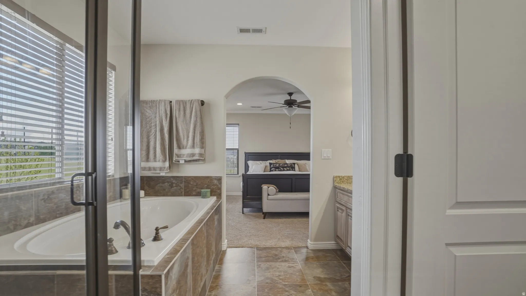 Ensuite bathroom with vanity, a shower stall, a garden tub, a ceiling fan, and dark stone finish flooring