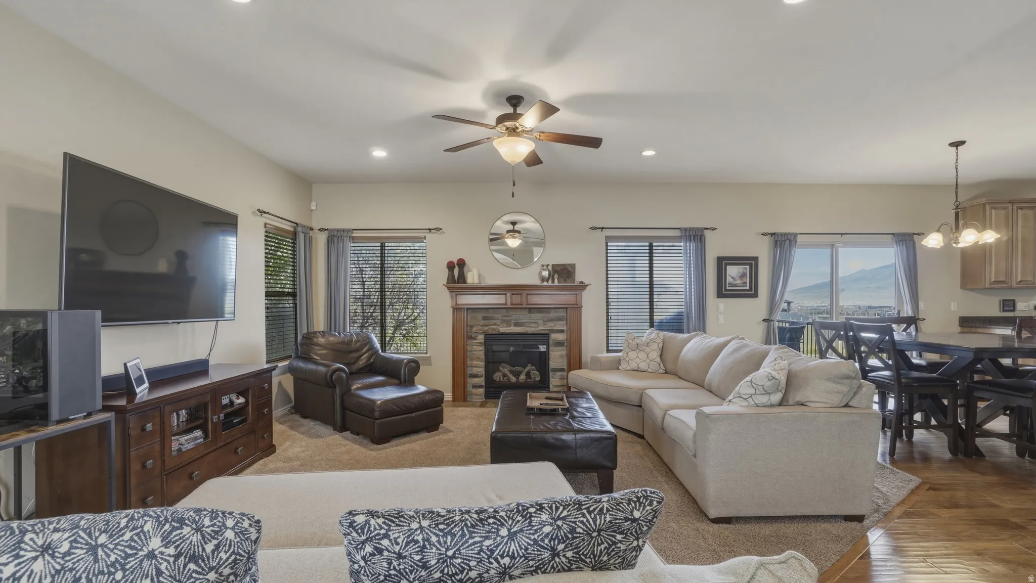 Living room featuring hanging lights, a stone fireplace, a ceiling fan, and wood finished floors