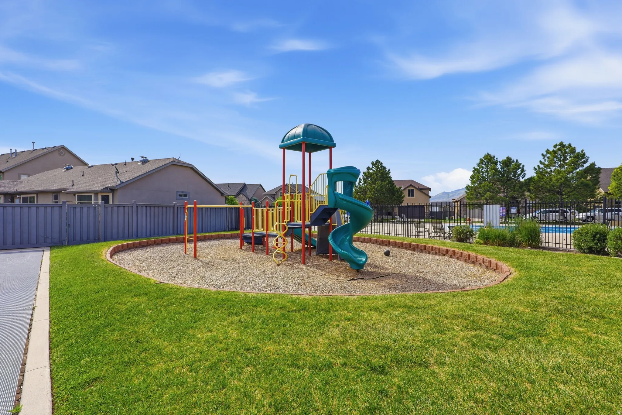 Community playground area featuring a colorful playset with slide and swings, surrounded by a manicured lawn