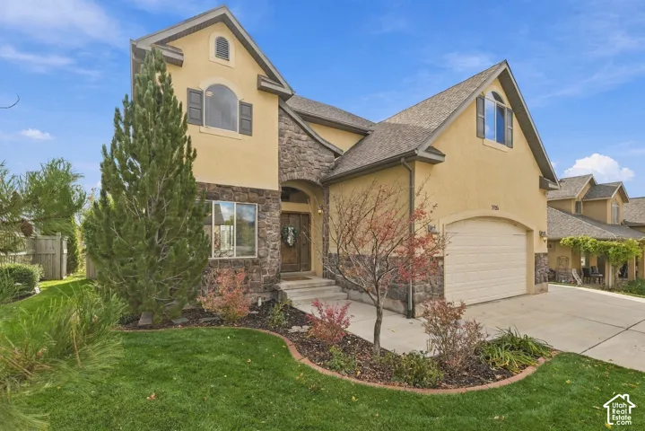 Multi-level exterior featuring stone veneer accents, stucco siding, arched window detailing, and a concrete driveway leading to an attached garage