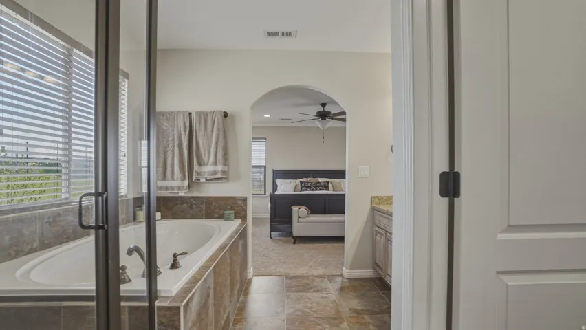 Ensuite bathroom with vanity, a shower stall, a garden tub, a ceiling fan, and dark stone finish flooring