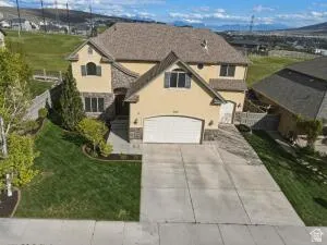 Two-story residence featuring a stucco and stone exterior, a two-car garage, concrete driveway, and landscaped front yard with mature plantings