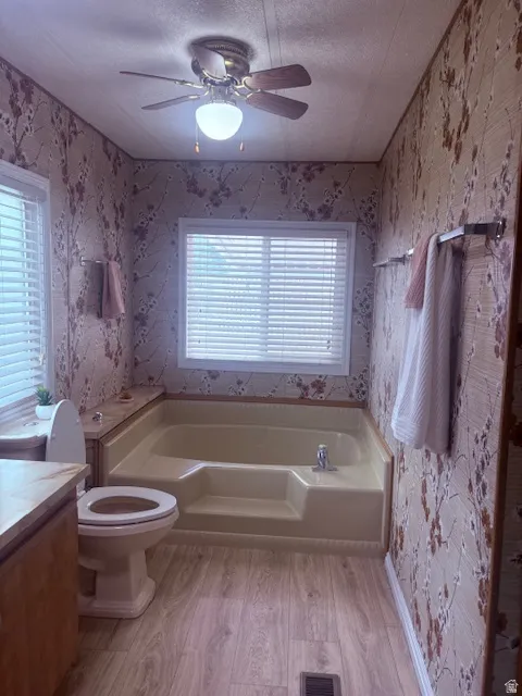 Bathroom with wallpapered walls, a textured ceiling, vanity, a bath, and light wood finished floors
