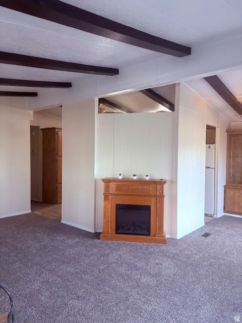 Unfurnished living room with beamed ceiling, carpet flooring, and a fireplace