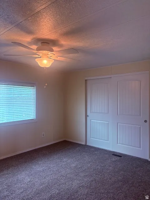 Unfurnished bedroom featuring a closet, carpet floors, ceiling fan, and a textured ceiling