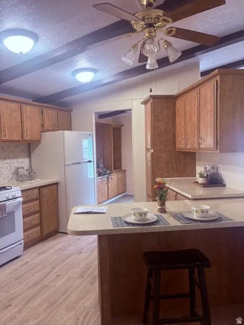 Kitchen featuring a textured ceiling, wood finish cabinets, white appliances, and light countertops