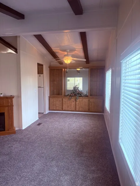 Unfurnished living room with carpet floors, a ceiling fan, vaulted ceiling with beams, a fireplace, and wooden walls