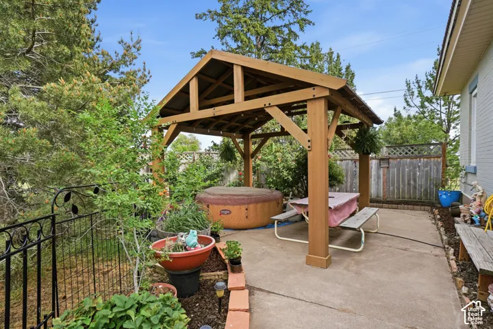 Concrete patio featuring a wood-frame gazebo, hot tub, and surrounding mature greenery