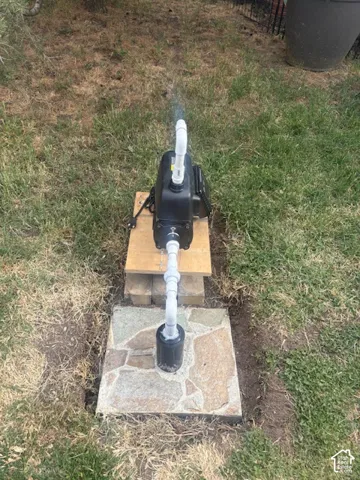 Pump for the well to water entire property Outdoor pump system with white PVC piping, positioned on a wooden base over a flagstone pad
