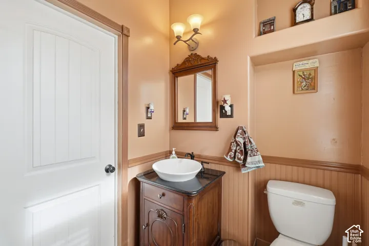 Bathroom featuring a white vessel sink, dark wood vanity with a black countertop, beadboard wainscoting, and a wall-mounted light fixture