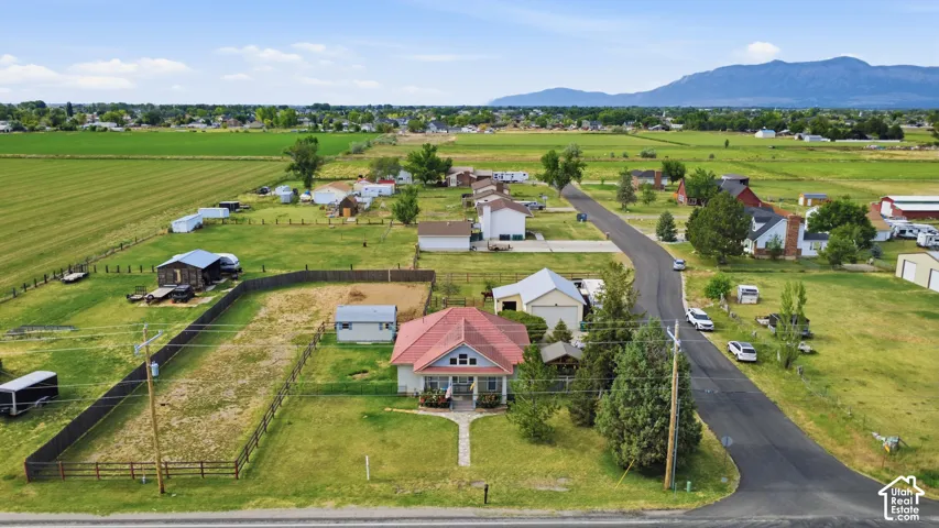 Aerial perspective showcasing a residential property with a red-roofed home, surrounded by green fields and distant mountains