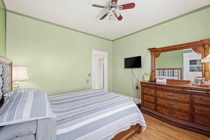 Room featuring light green walls with a darker green crown molding, wood-finish flooring, and a ceiling fan