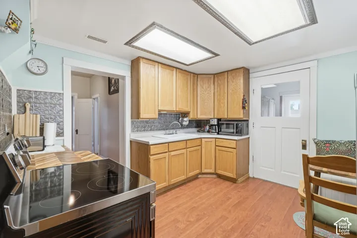 Kitchen featuring wood-finish flooring, natural wood cabinetry, a white countertop, and a pressed tin-look backsplash