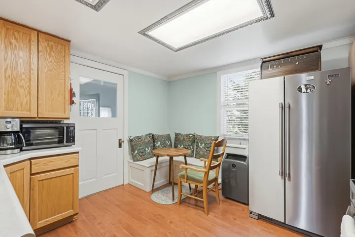 Kitchen featuring wood-finish flooring, light wood cabinetry, a built-in bench, stainless steel refrigerator, and a ceiling-mounted light fixture