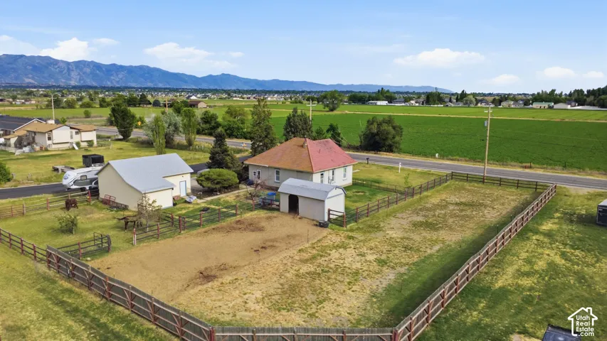Expansive property featuring a main residence with a red roof, a separate accessory building with a gray roof, a smaller shed, and fenced pasture areas