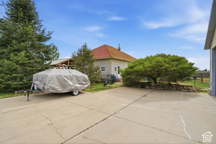 Spacious concrete parking pad with mature evergreen trees and a substantial shade tree