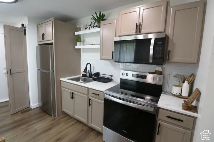 Kitchen with stainless steel appliances, open shelves, dark wood-style floors, decorative backsplash, and light stone counters