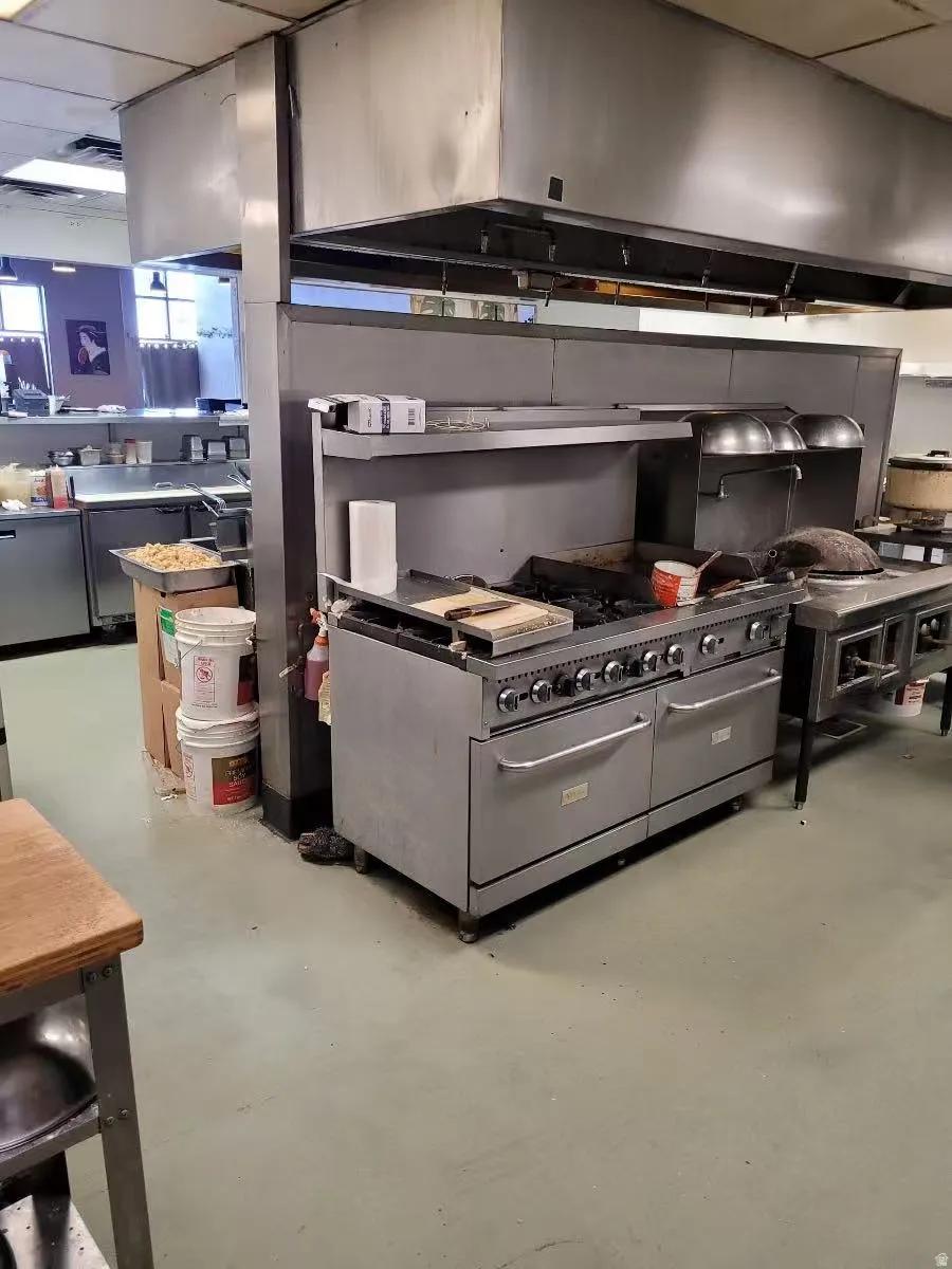Kitchen with exhaust hood, double oven range, a drop ceiling, and concrete floors